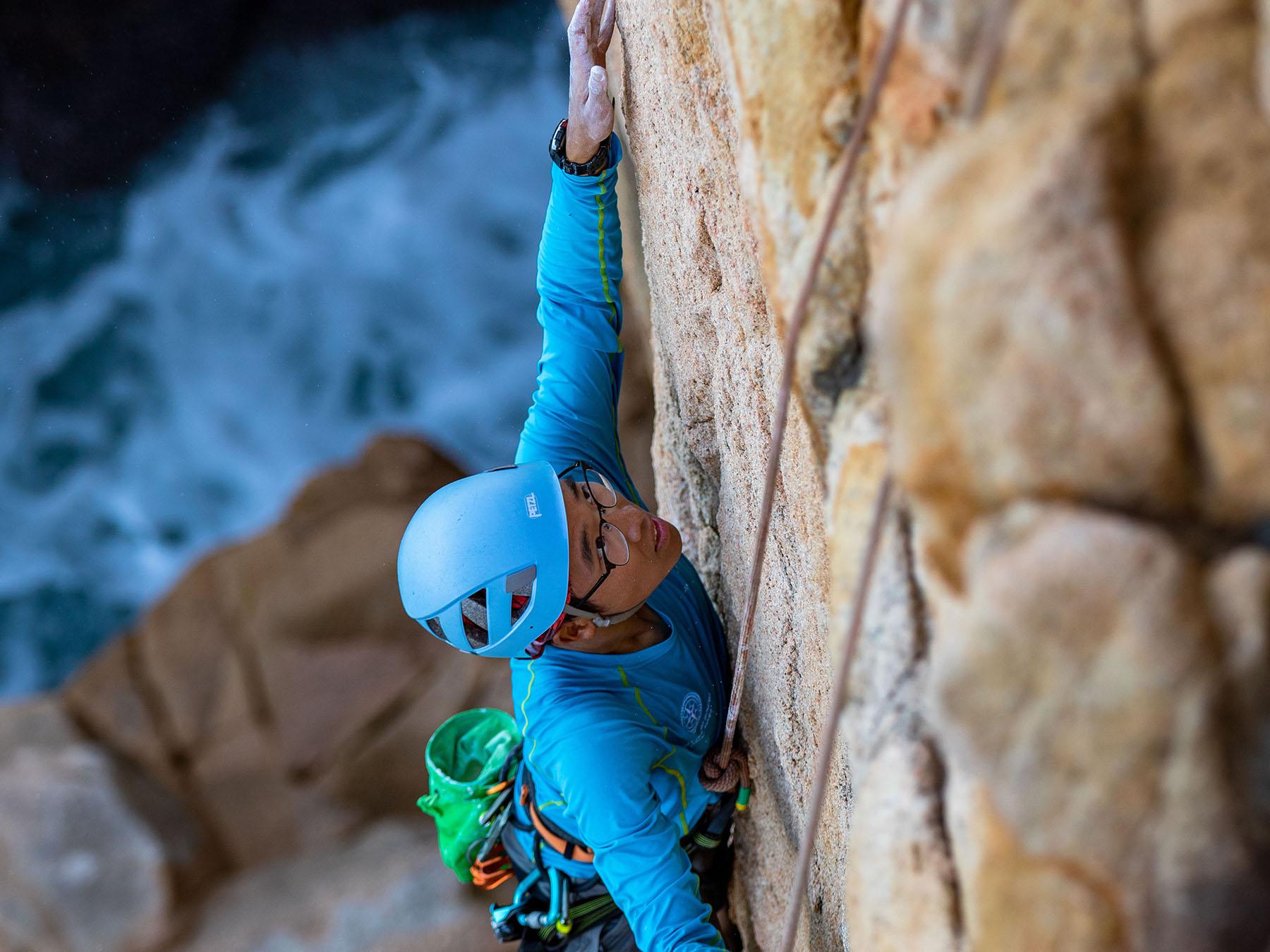 Outward Bound student climbing up sheer rock face with rocks and the sea below.