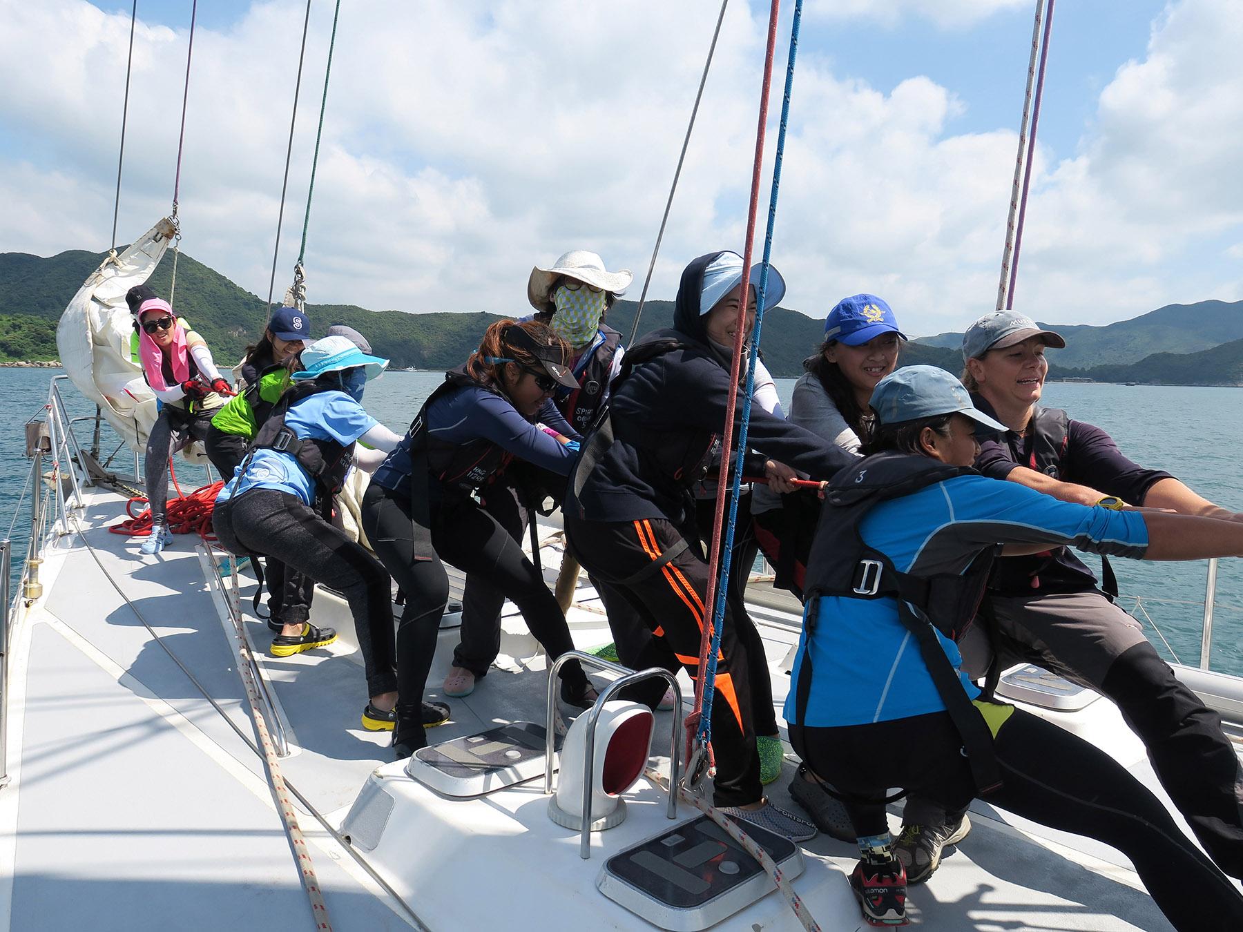 About a dozen Outward Bound pull a rope on a sailboat