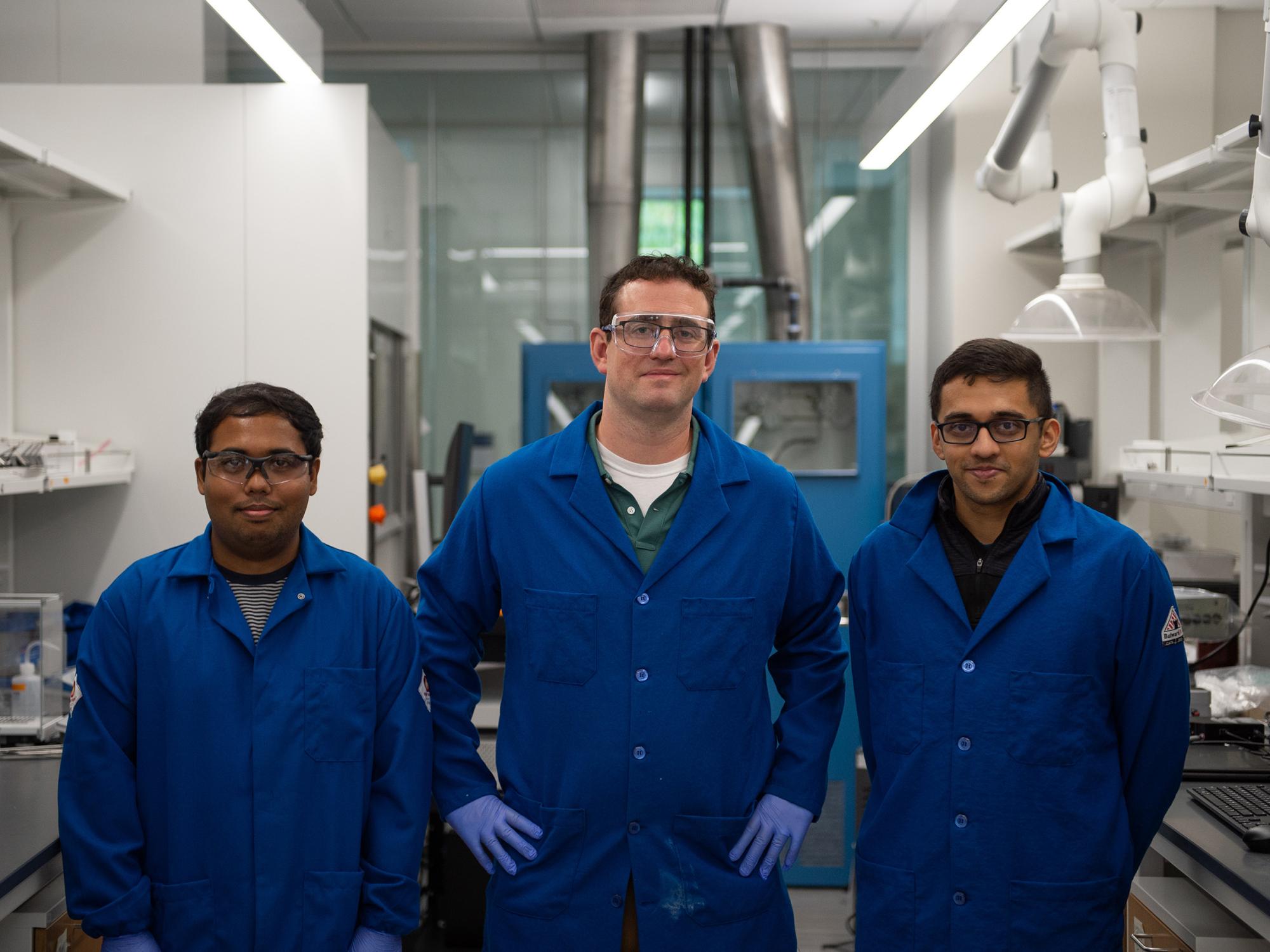 Three individuals wearing lab coats pose in a lab.