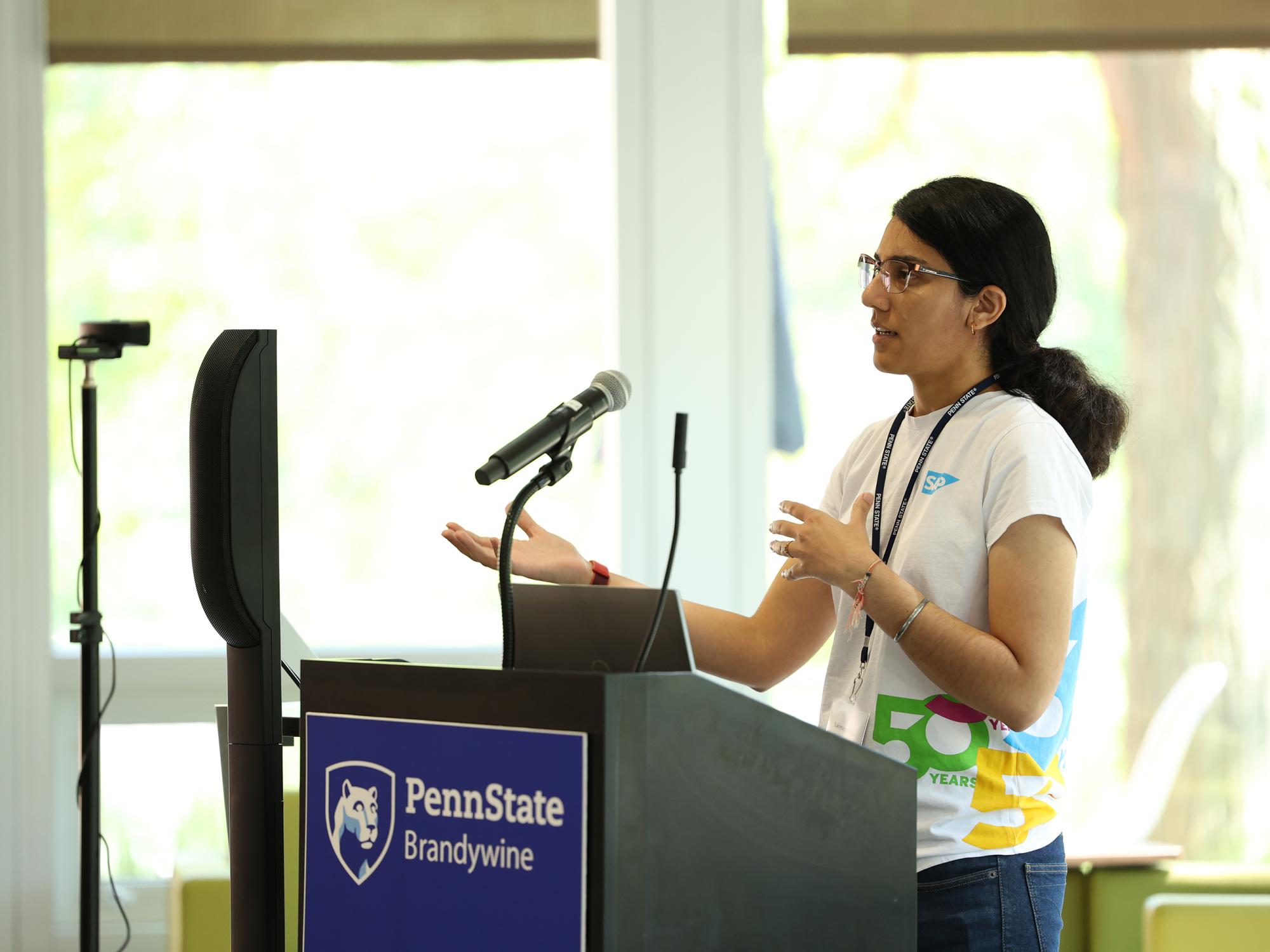 A woman speaks to an audience next to a lectern.