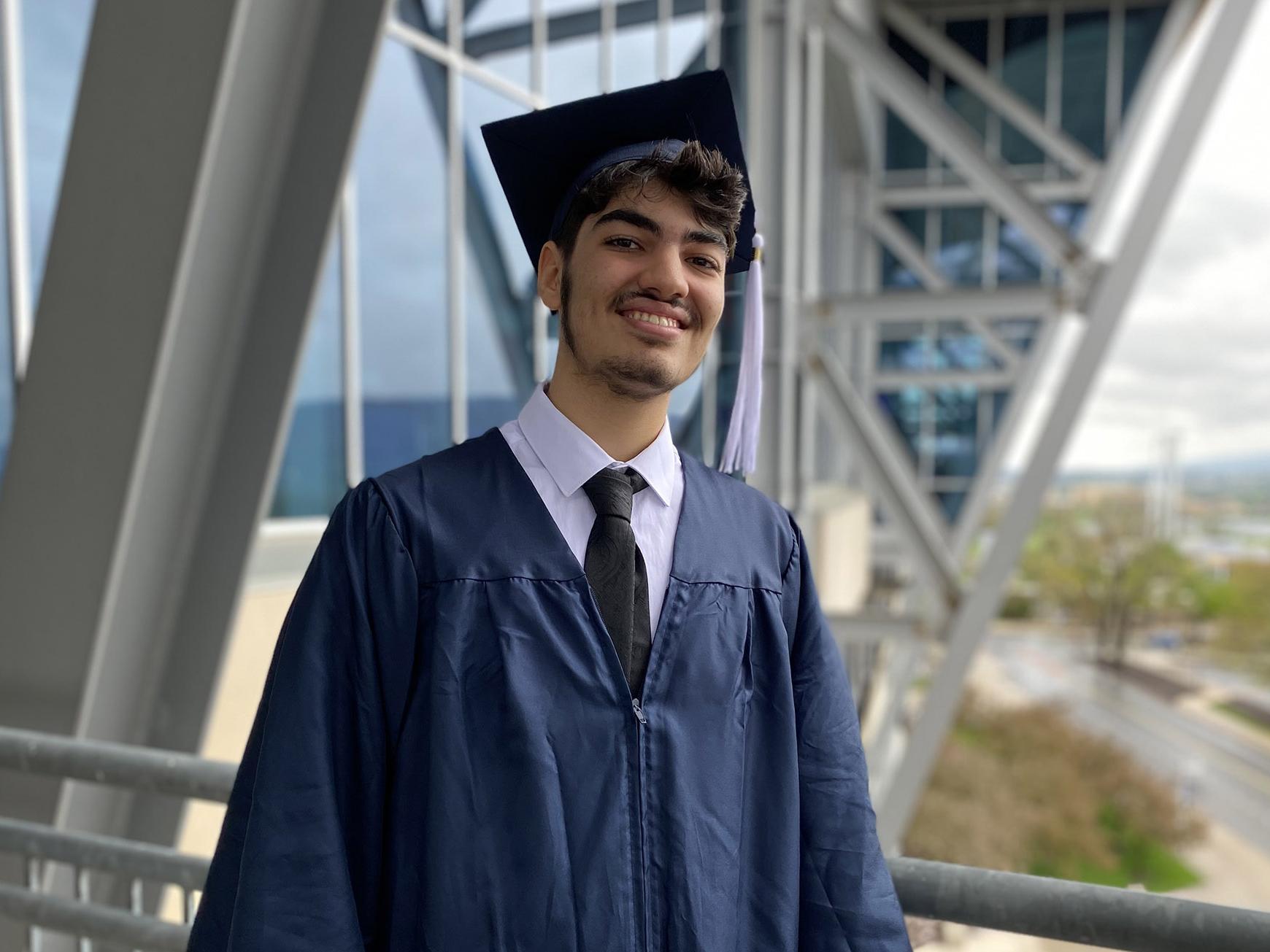 AbdAllah Mahassen is dressed in a cap and gown and stands with Beaver Stadium in the background
