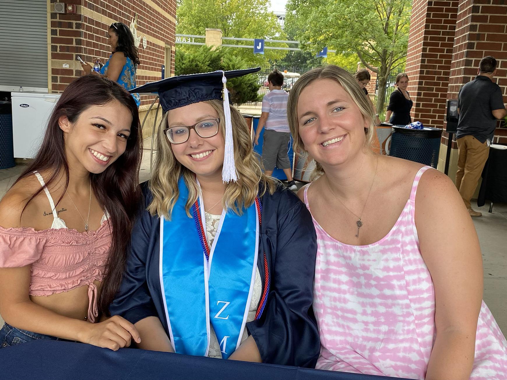 Jona Hall sits at a table with two friends at the Penn State World Campus Graduation Celebration in summer 2021.