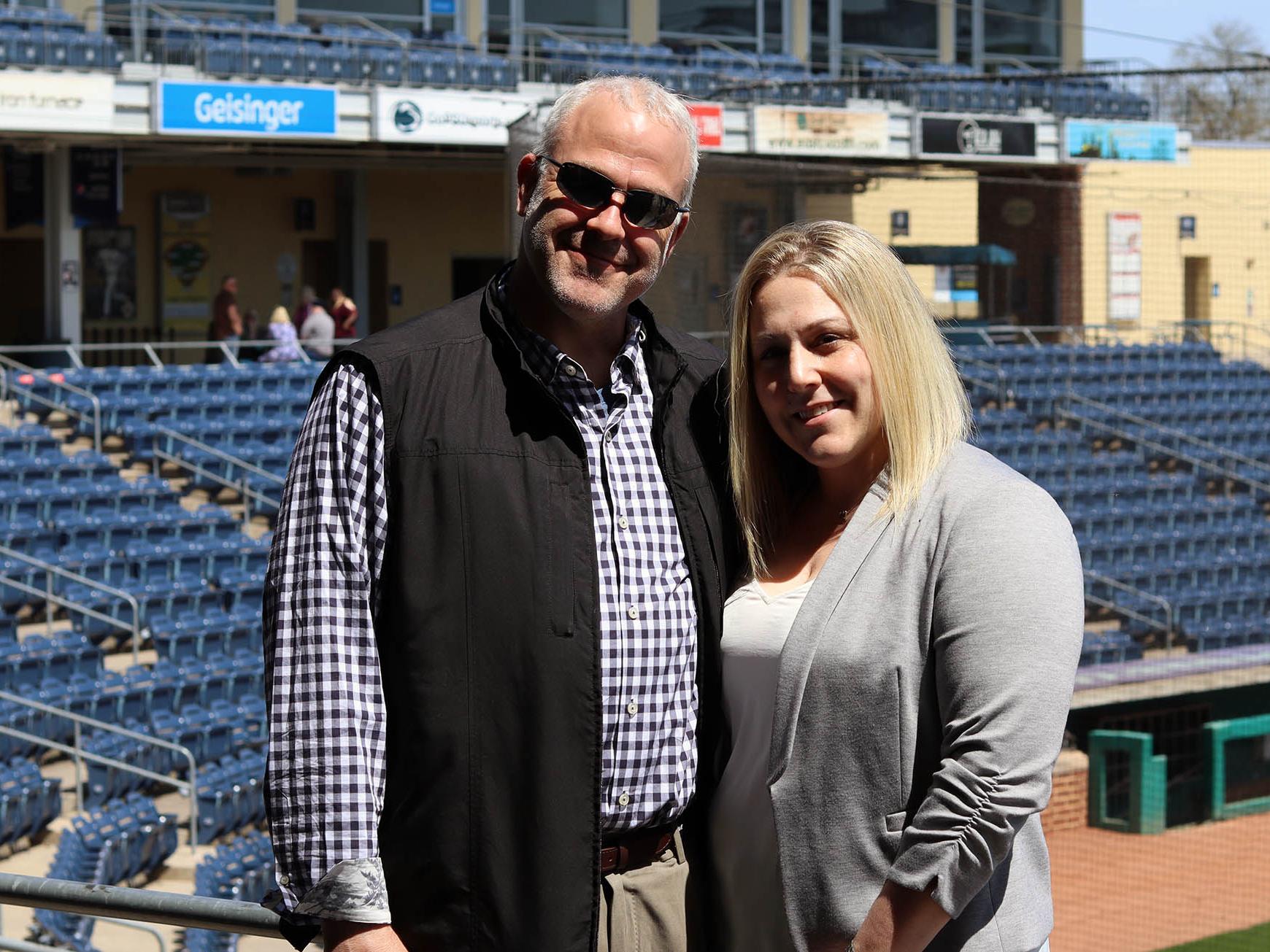 Victoria Freed stands with her husband with baseball stadium seats in the background