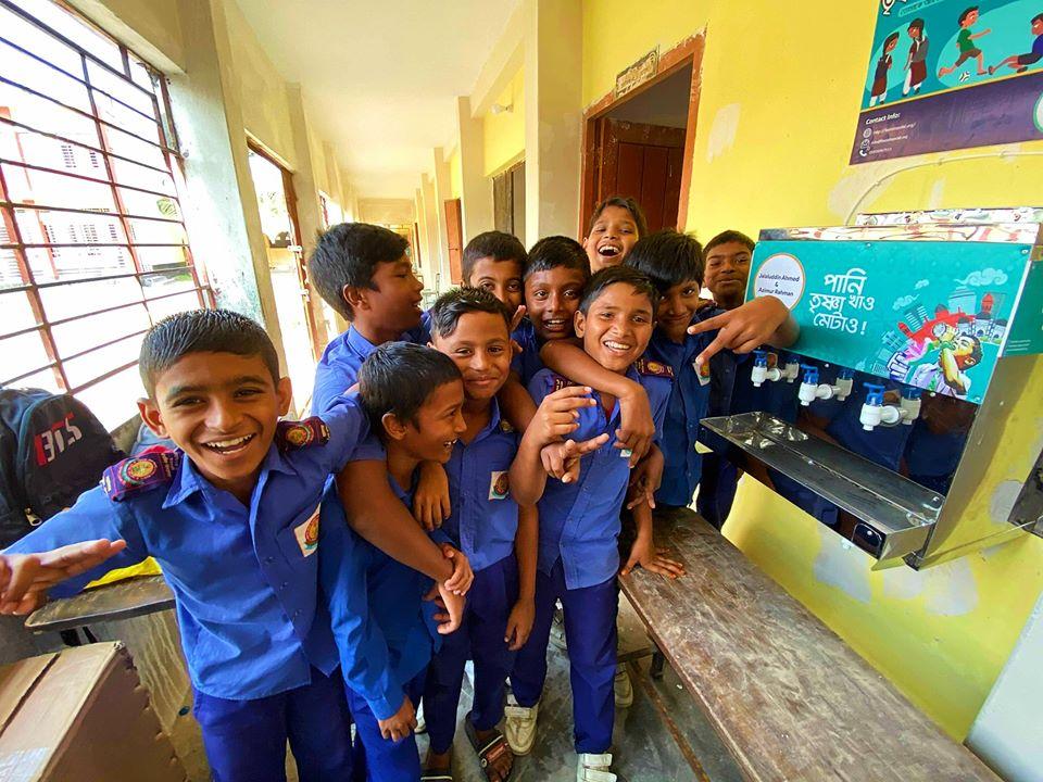 A group of children smiling and gathered around a water system