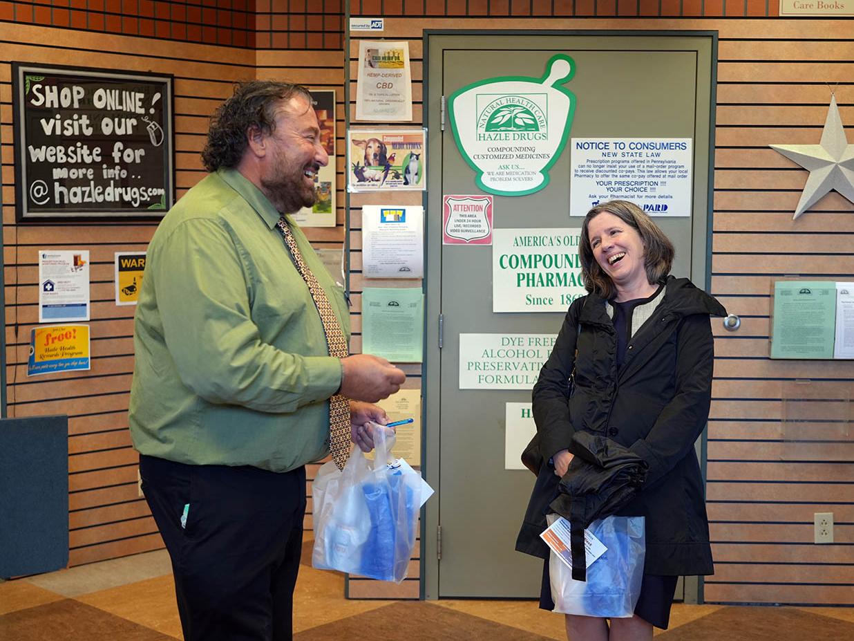 Man and woman laughing during conversation inside a pharmacy waiting area.