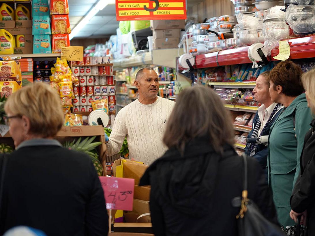 Grocery store owner speaking to group of people gathered inside store.
