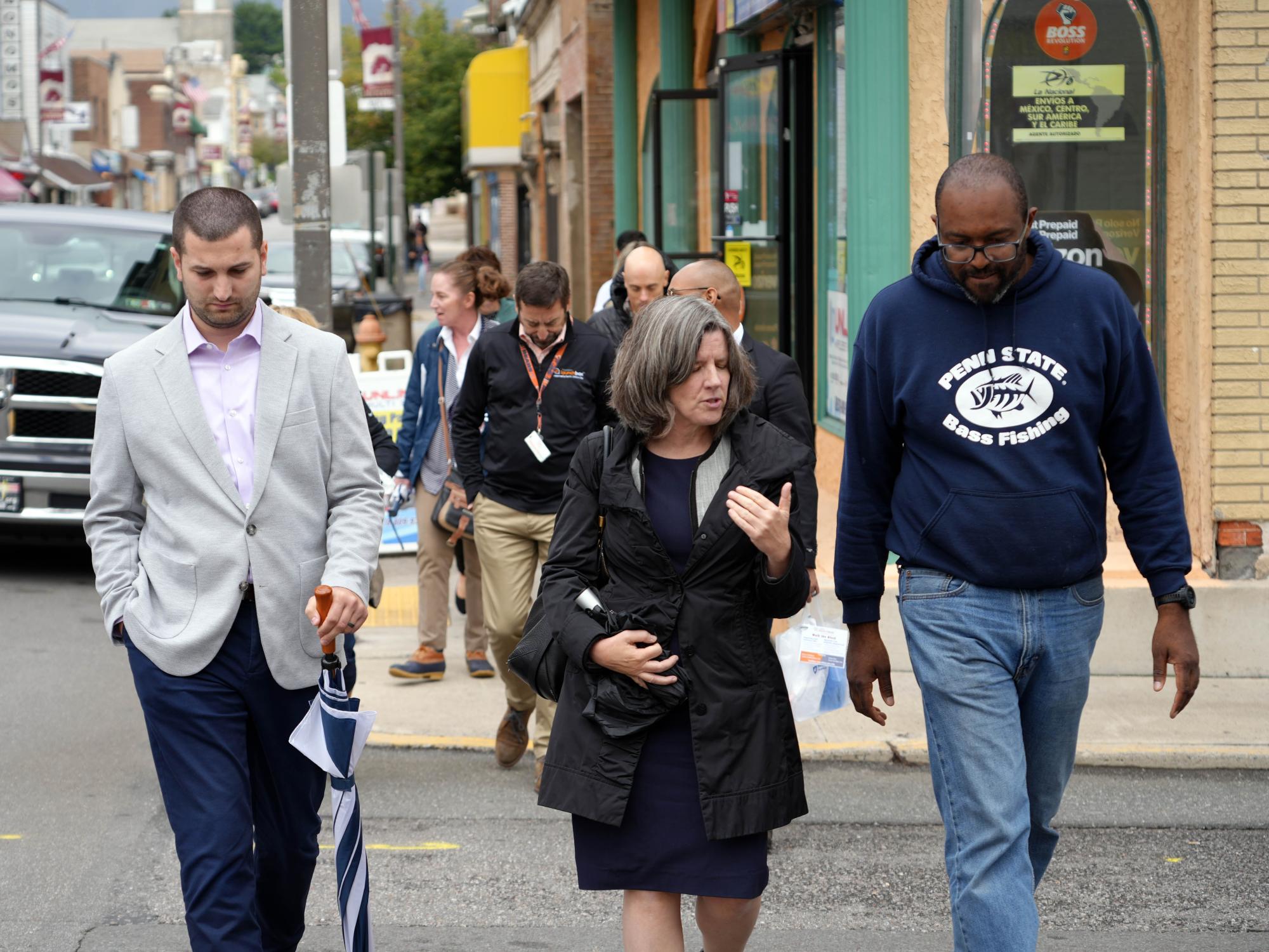 Three people smiling and walking together across a downtown street.