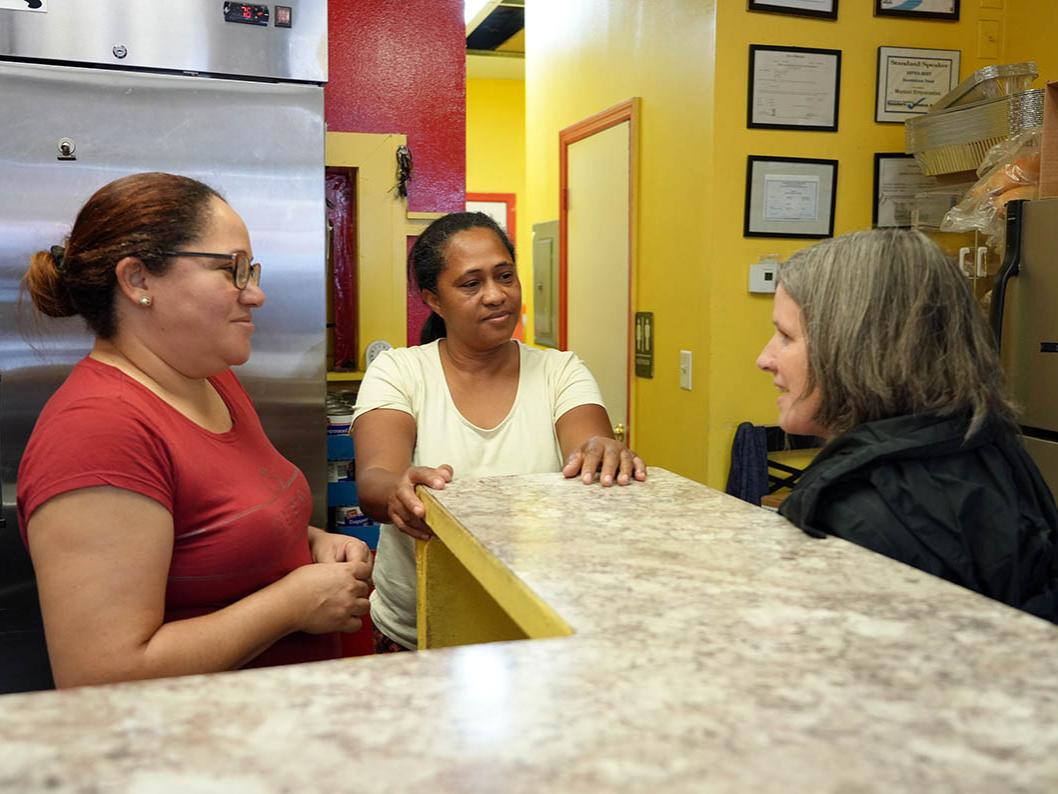 Female talking to two business owners from across the counter.