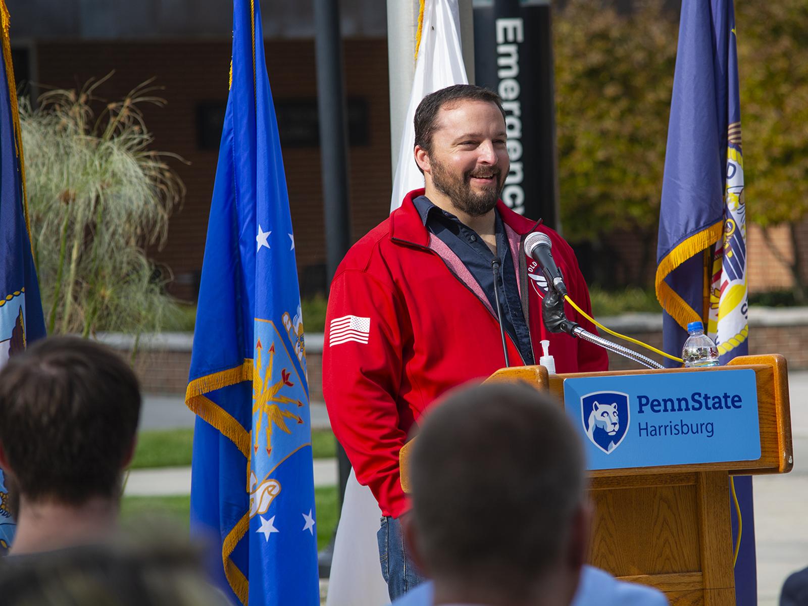 Photo of Ryan Allman, standing behind a lecturn and in front of flags during a 2021 Veterans Day ceremony 