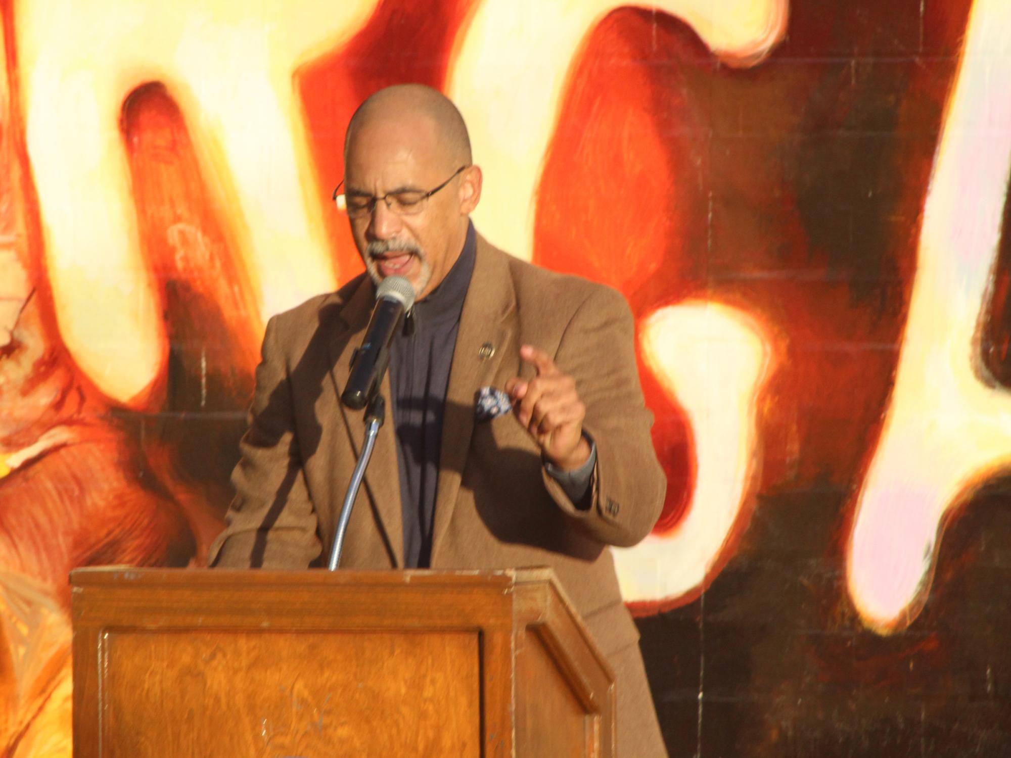  A person standing at a podium with a colorful red and orange mural behind them