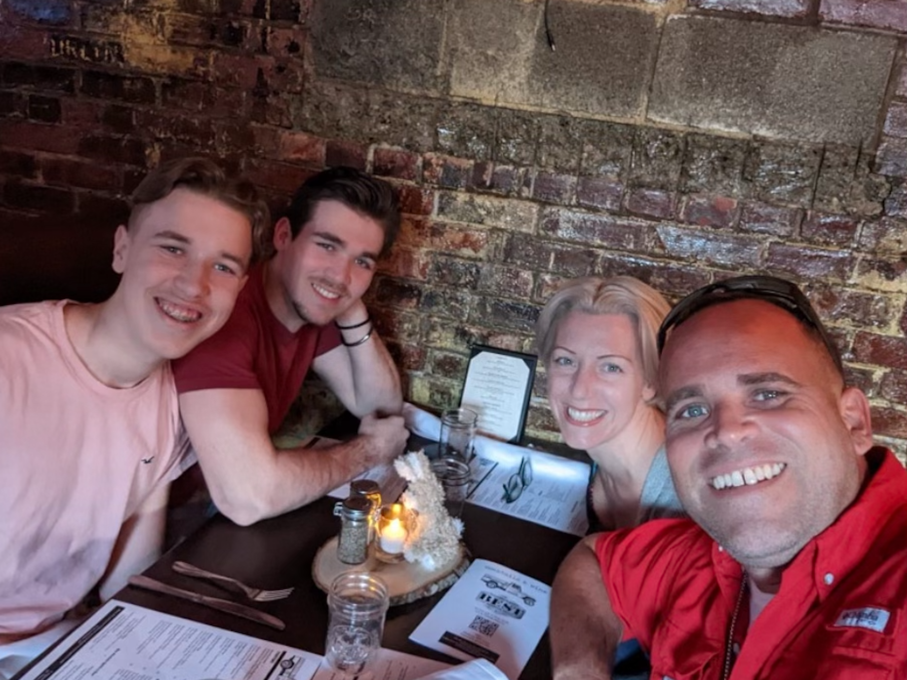 Tyler Vazquez (second from left) sits with his family at a table against a brick wall in a New York restaurant.