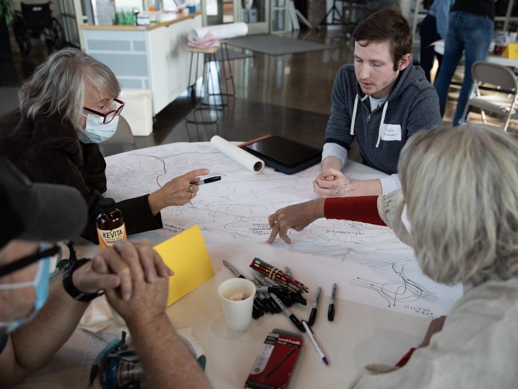 A Penn State landscape architecture student sits at a table with local residents during the community design charrette with maps of the area and plans for other design options laid before them.