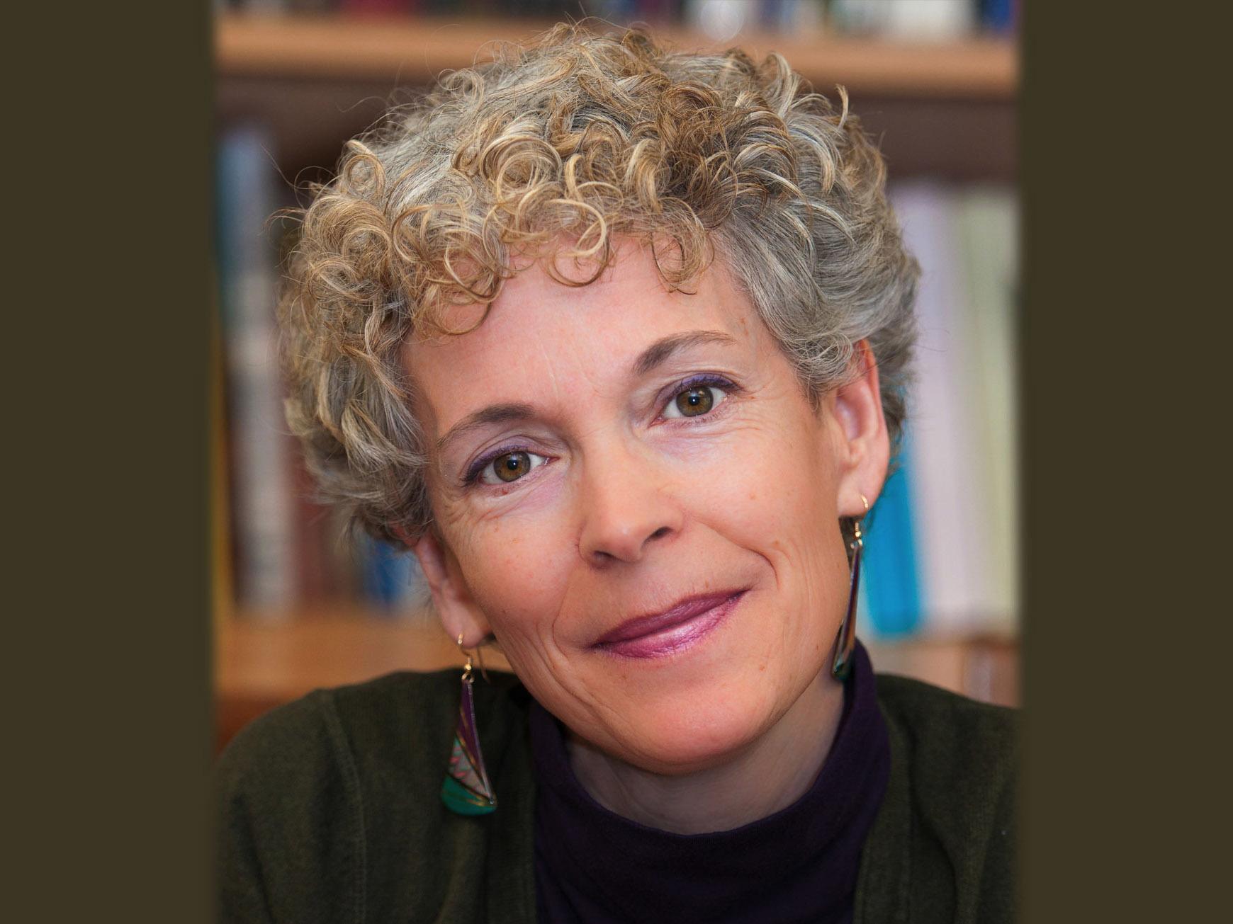 Judy McKelvey poses for a photo with a bookcase and books in the background