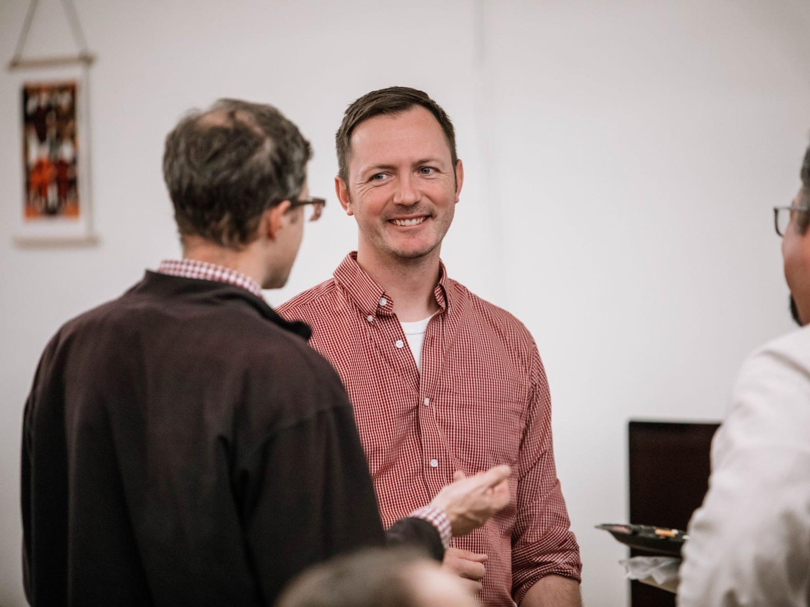 Man smiles as another man talks
