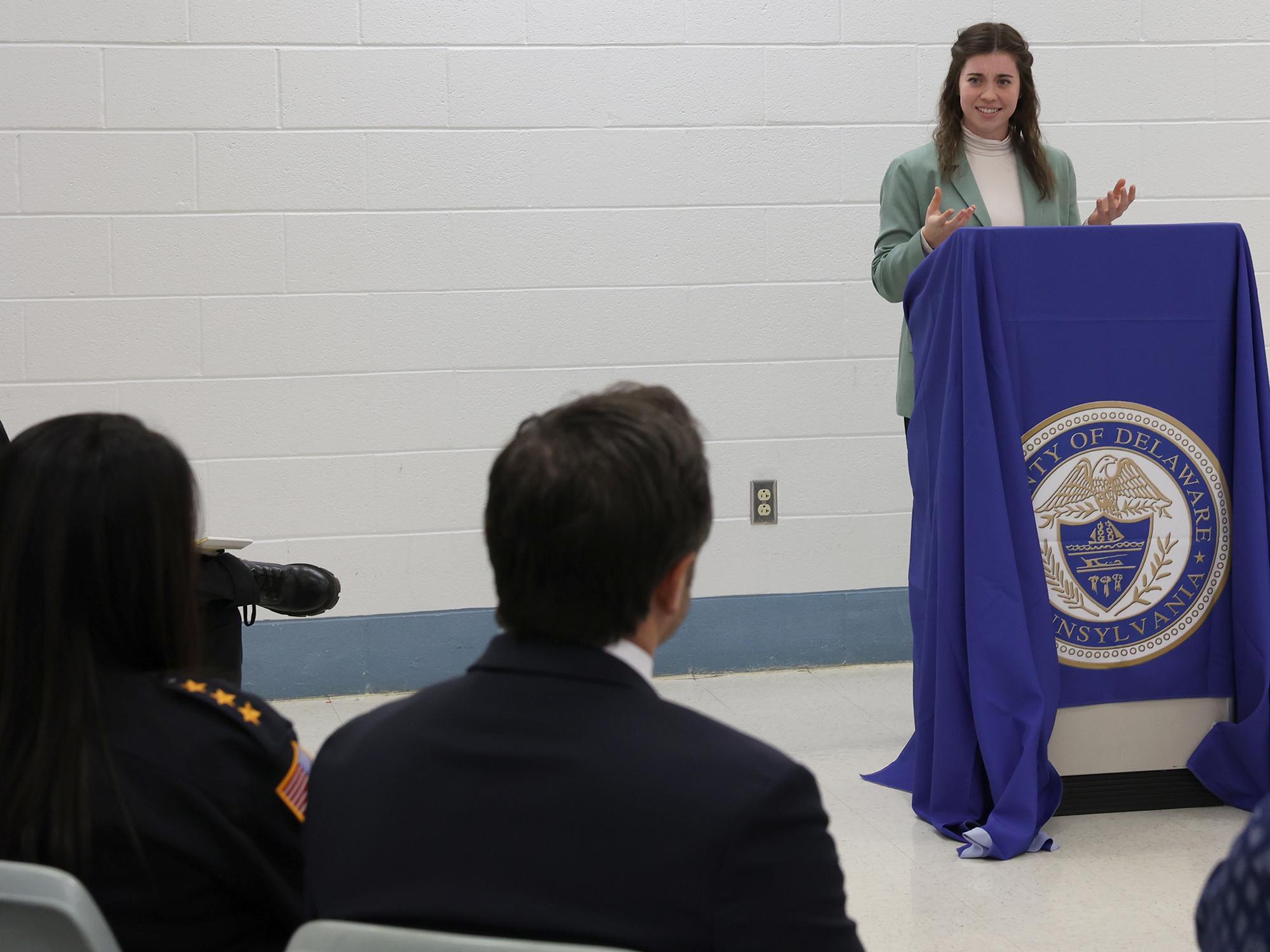 A woman stands at a lectern and speaks to a group of people seated.