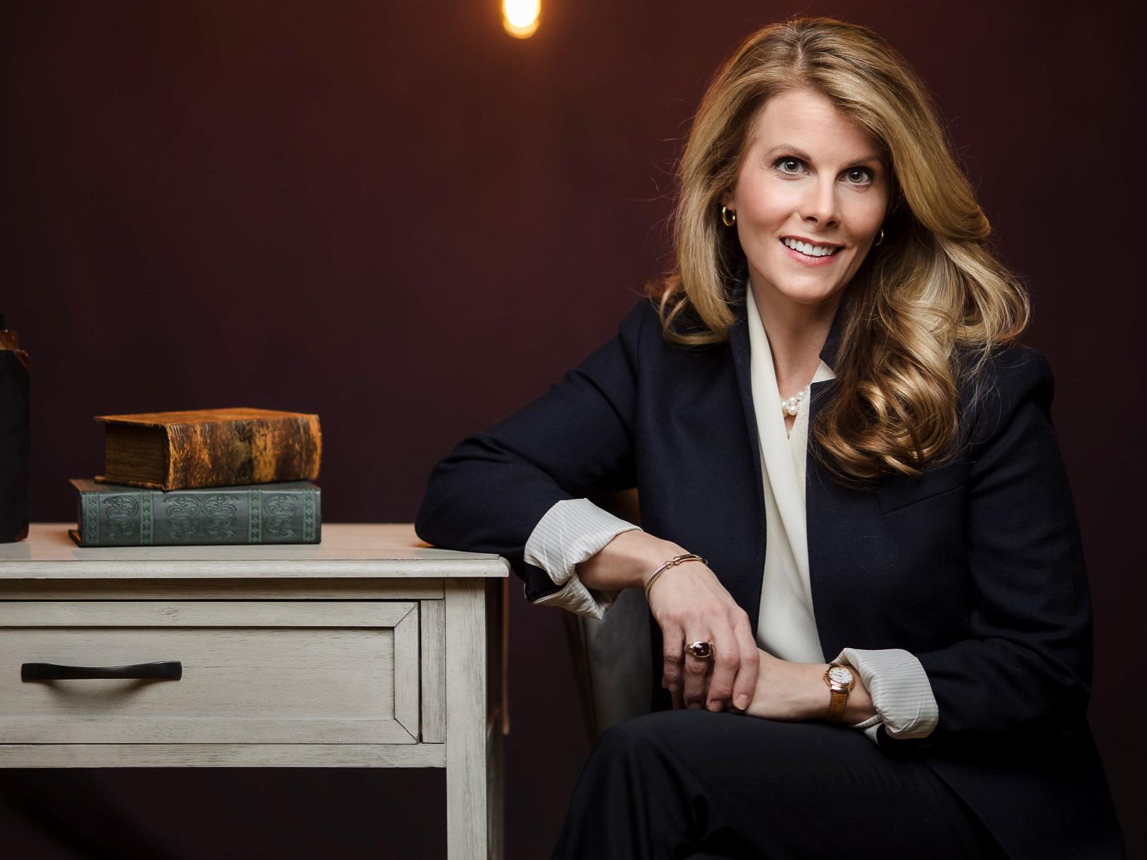 A portrait of Erica Monaghan who is seated next to an end table with two books on it