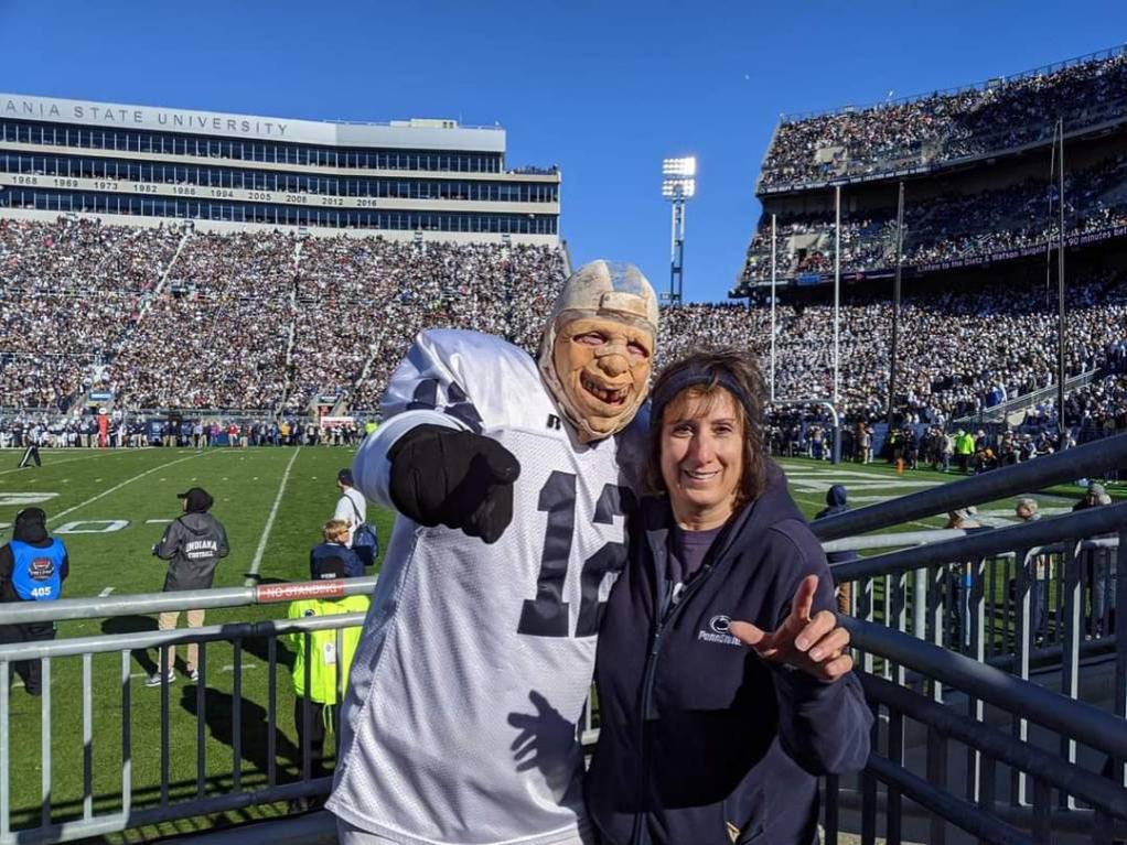 Theresa Tama poses with someone dressed as a football player, No. 12, with the stands of Beaver Stadium in the background.