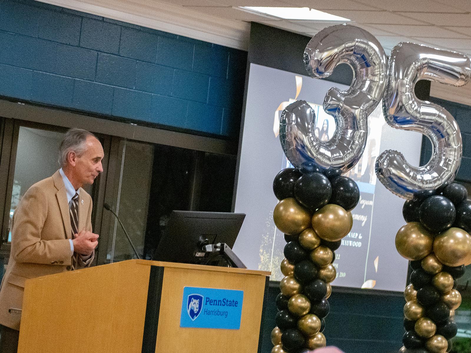 Penn State Harrisburg Chancellor John M. Mason Jr. speaks during the anniversary celebration for the Multicultural Academic Excellence Program. Large balloons shaped like the number 35 are in the background.