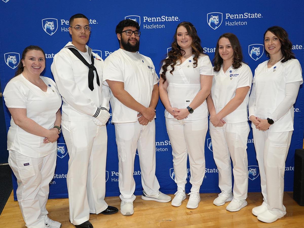 Group of six practical nursing graduates in white scrubs.