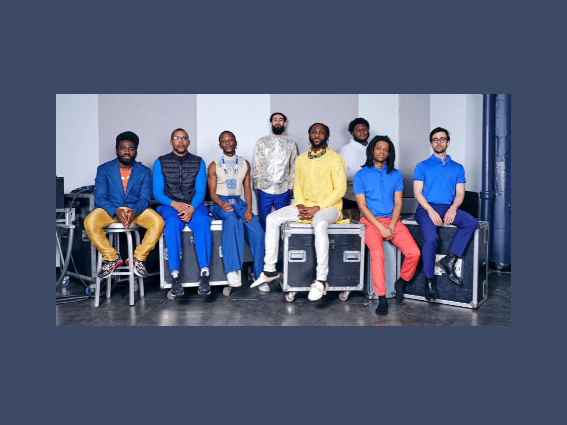 A diverse group of men of color sit atop musical equipment cases.