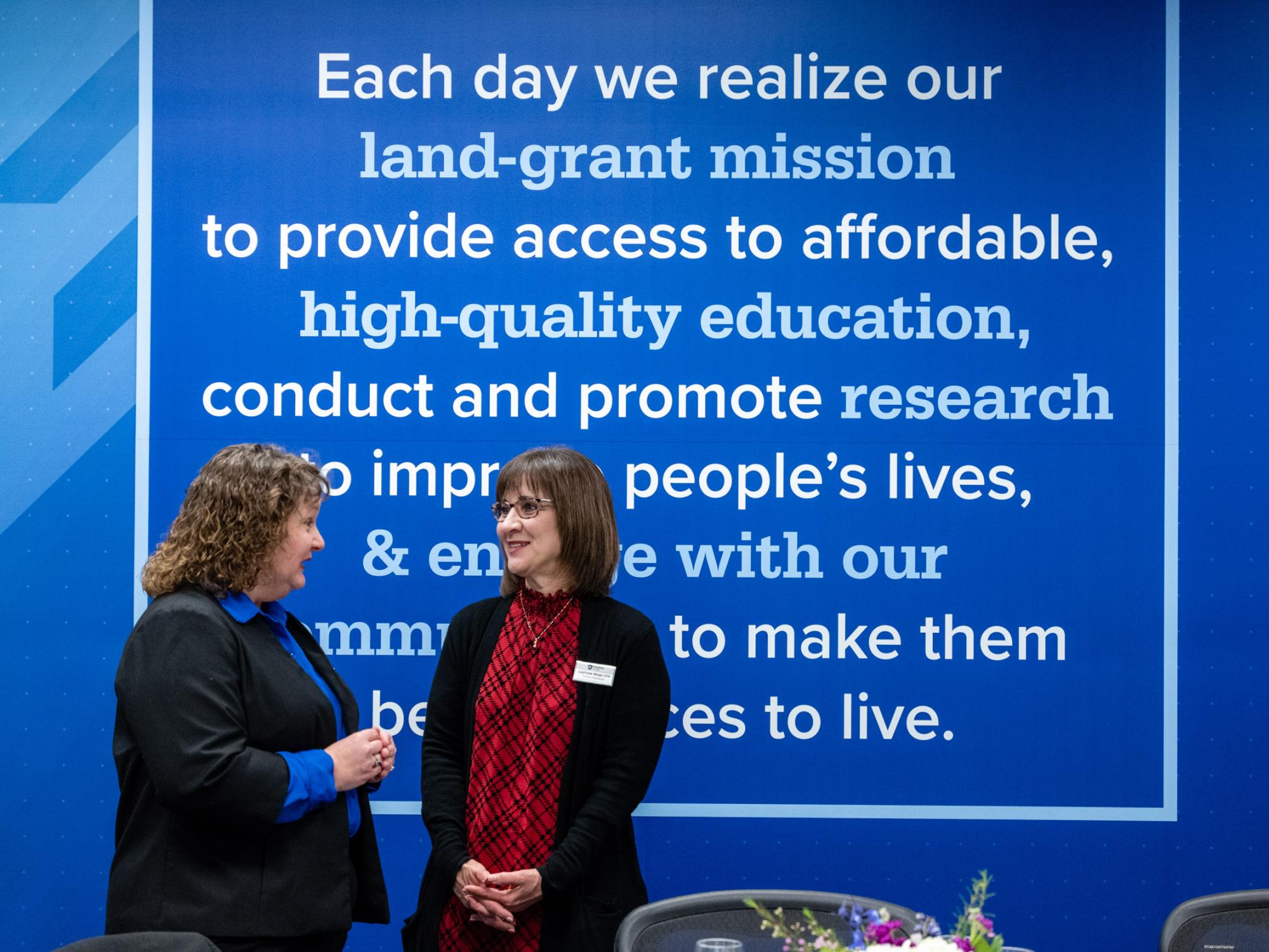 Two women talk in front of a blue wall