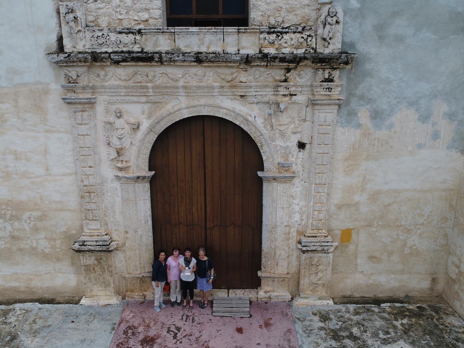 Aerial photo of three tiny figures standing in front of an old monastery.