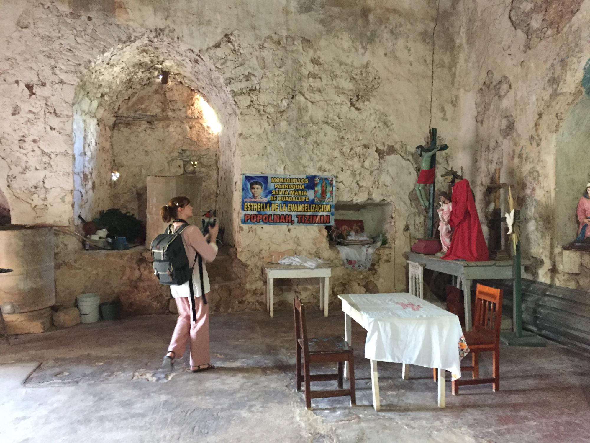 Woman in old church holding camera looks at paintings on wall.