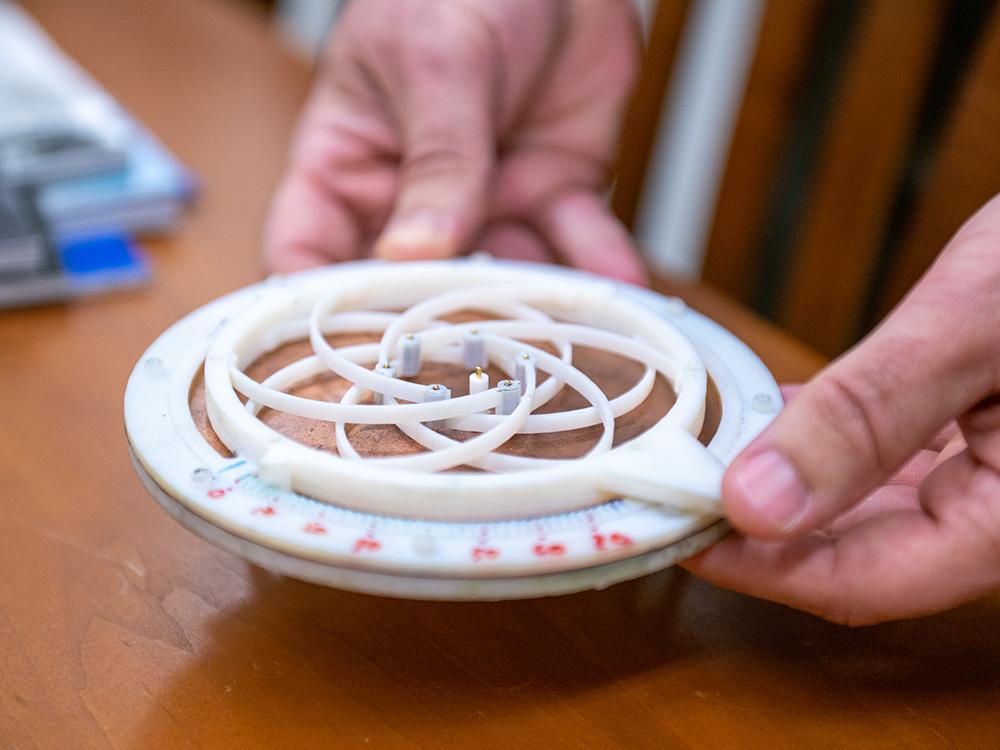 A small, circular, white and tan antenna prototype is displayed on a table. 