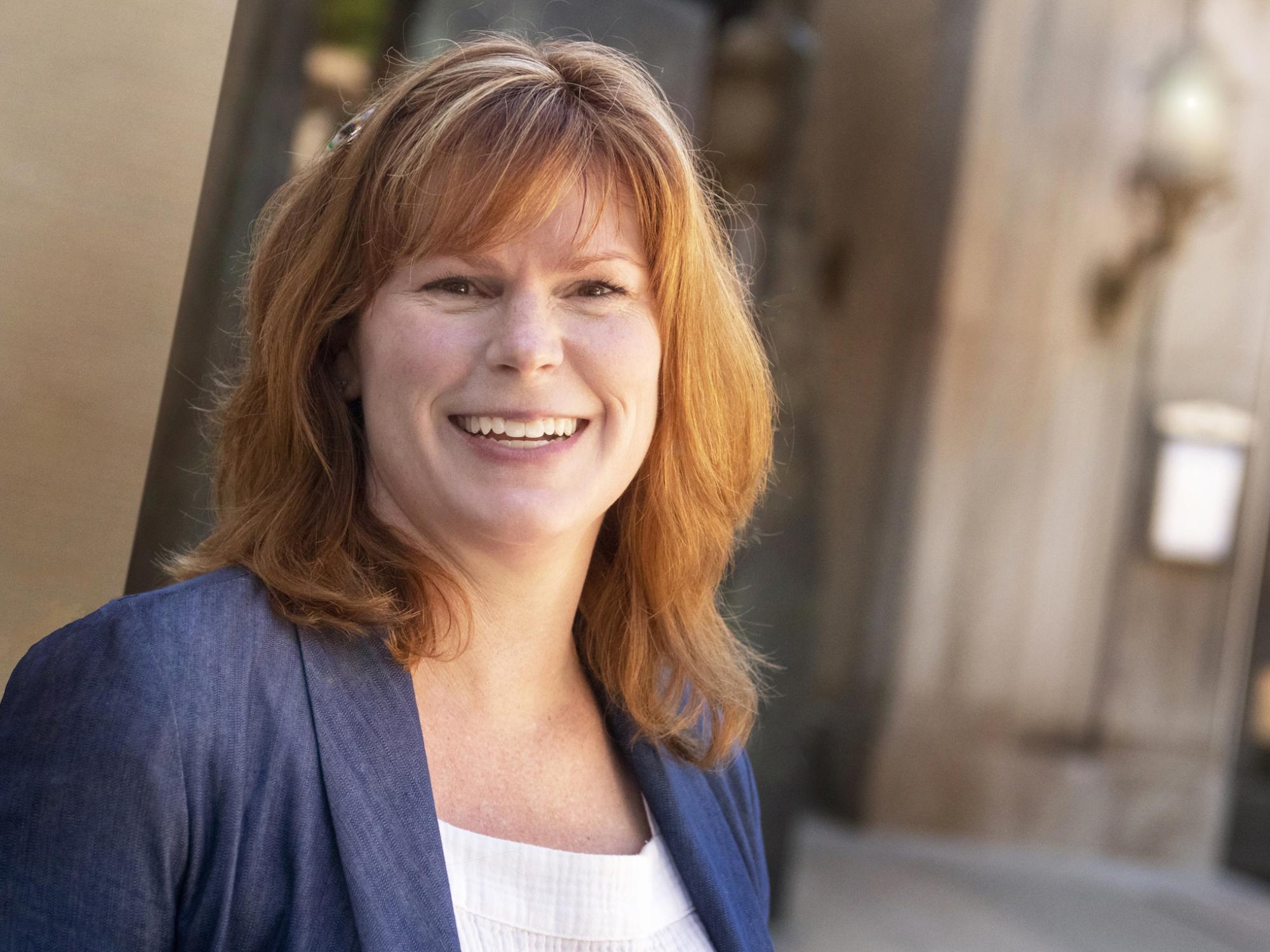 Red-haired woman in blue jacket smiling toward camera