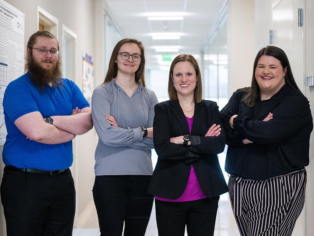 Four people stand in a hallway, facing the camera.