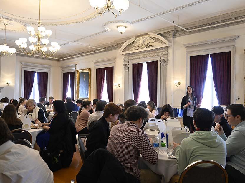 Groups of students seated around tables listening to a speaker