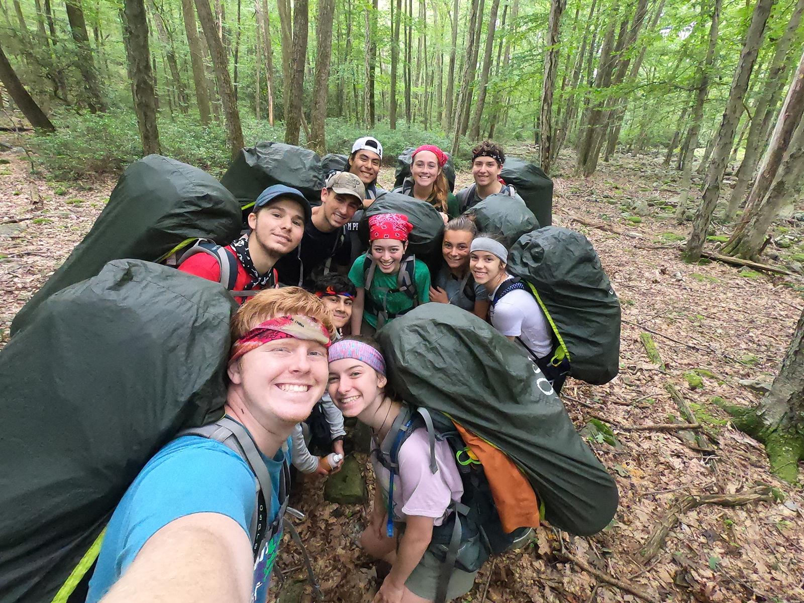 A group of students out hiking in the woods smile for a selfie