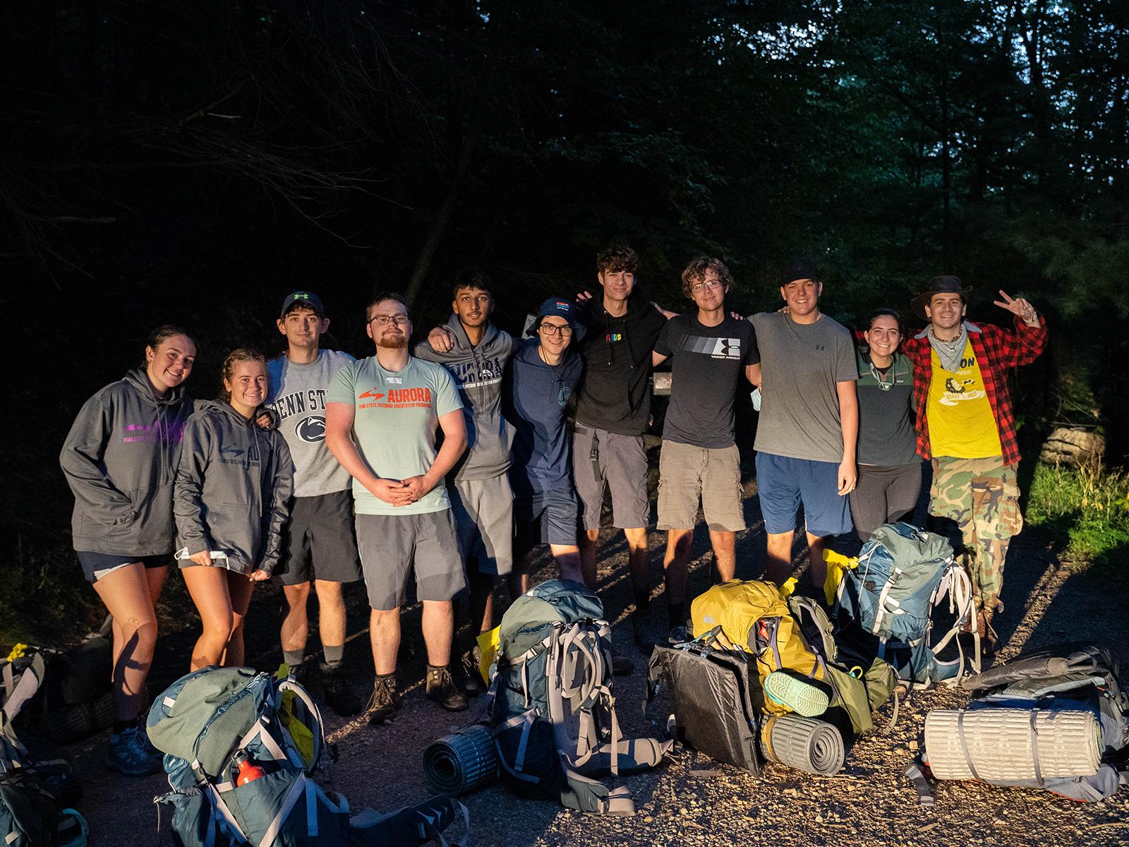 A group of students in the woods at night standing with their camping gear