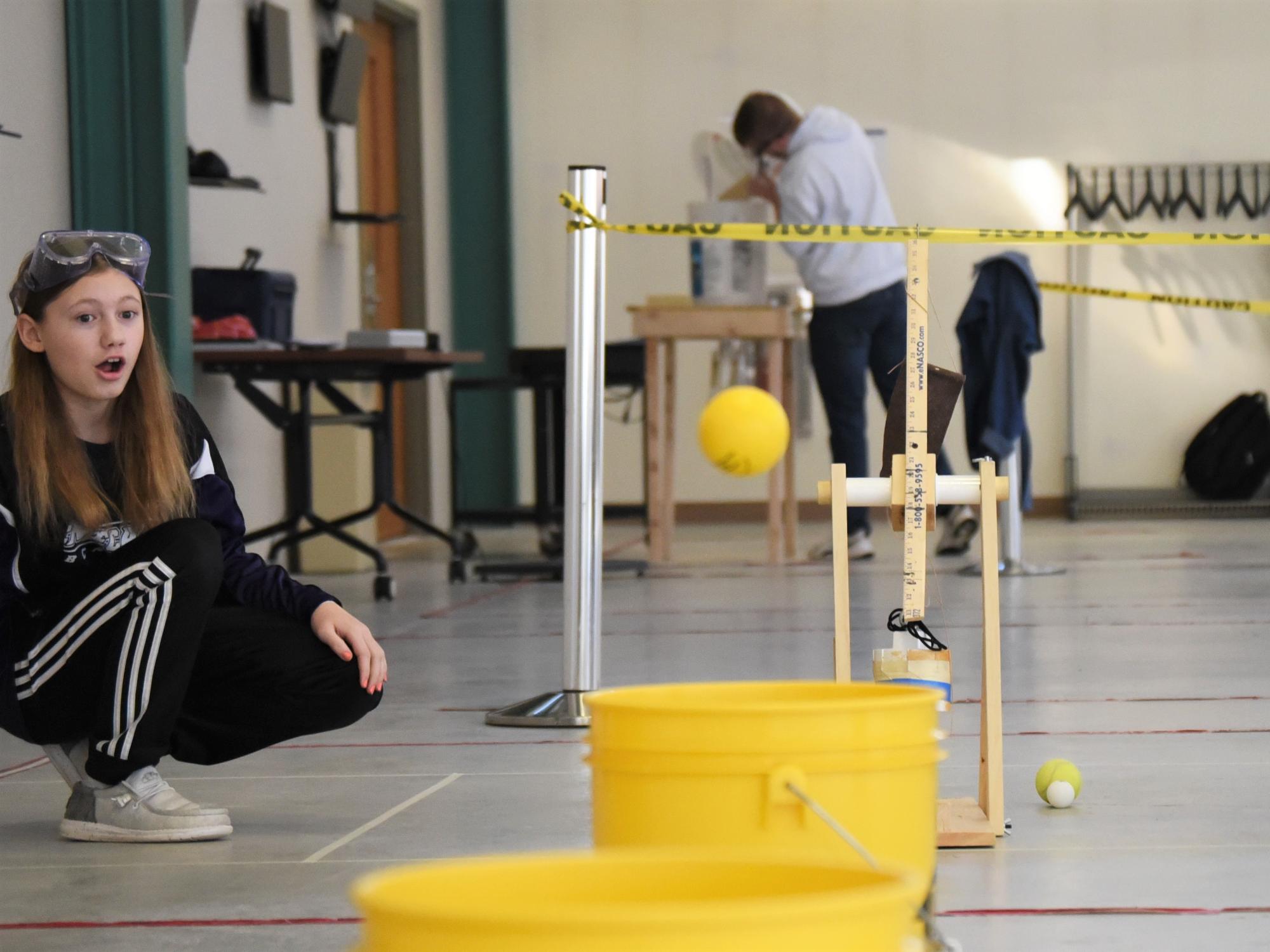 A female student watches a rubber ball fly toward a bucket at the Science Olympiad at Penn State Behrend.