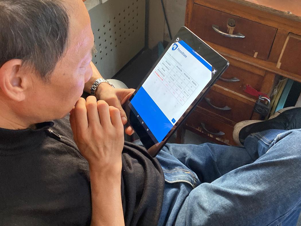 A man sits at a desk holding a tablet that has a Penn State-branded survey on the screen. 