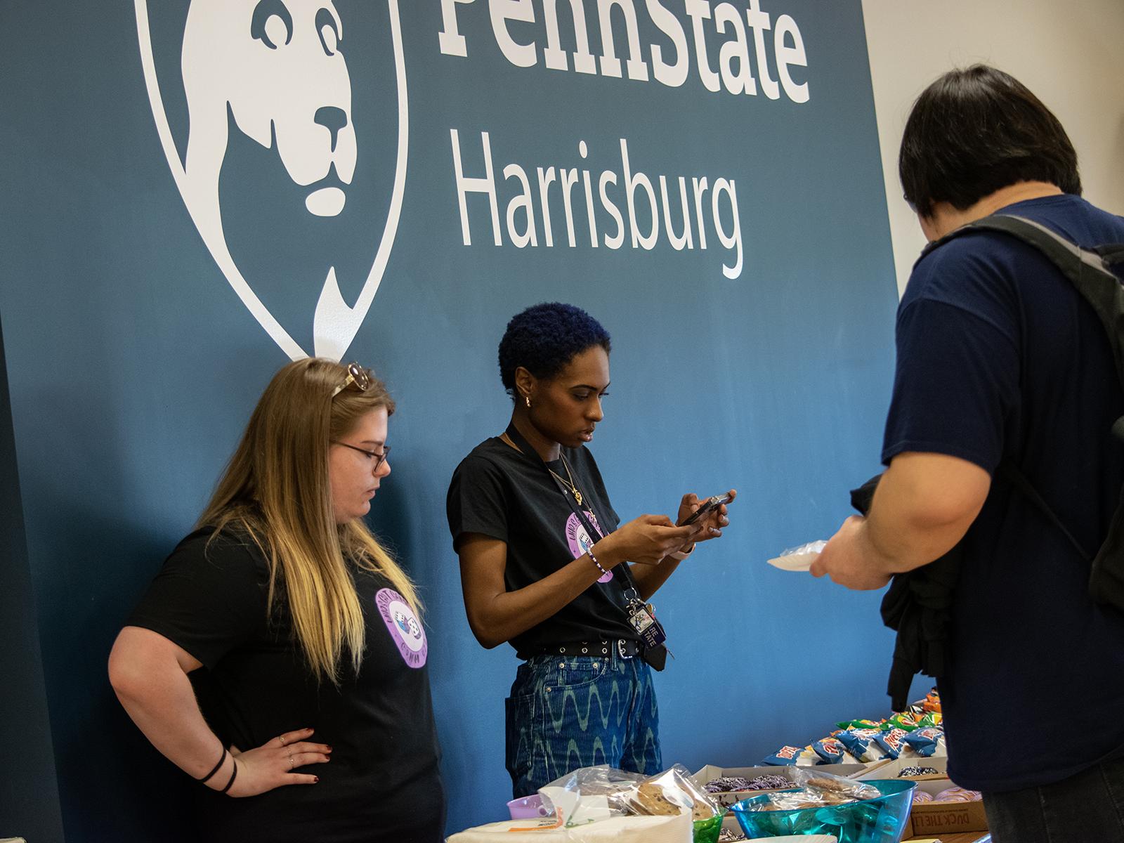 Two students stand behind a snack table, while another student gets a snack, during a game night fundraiser