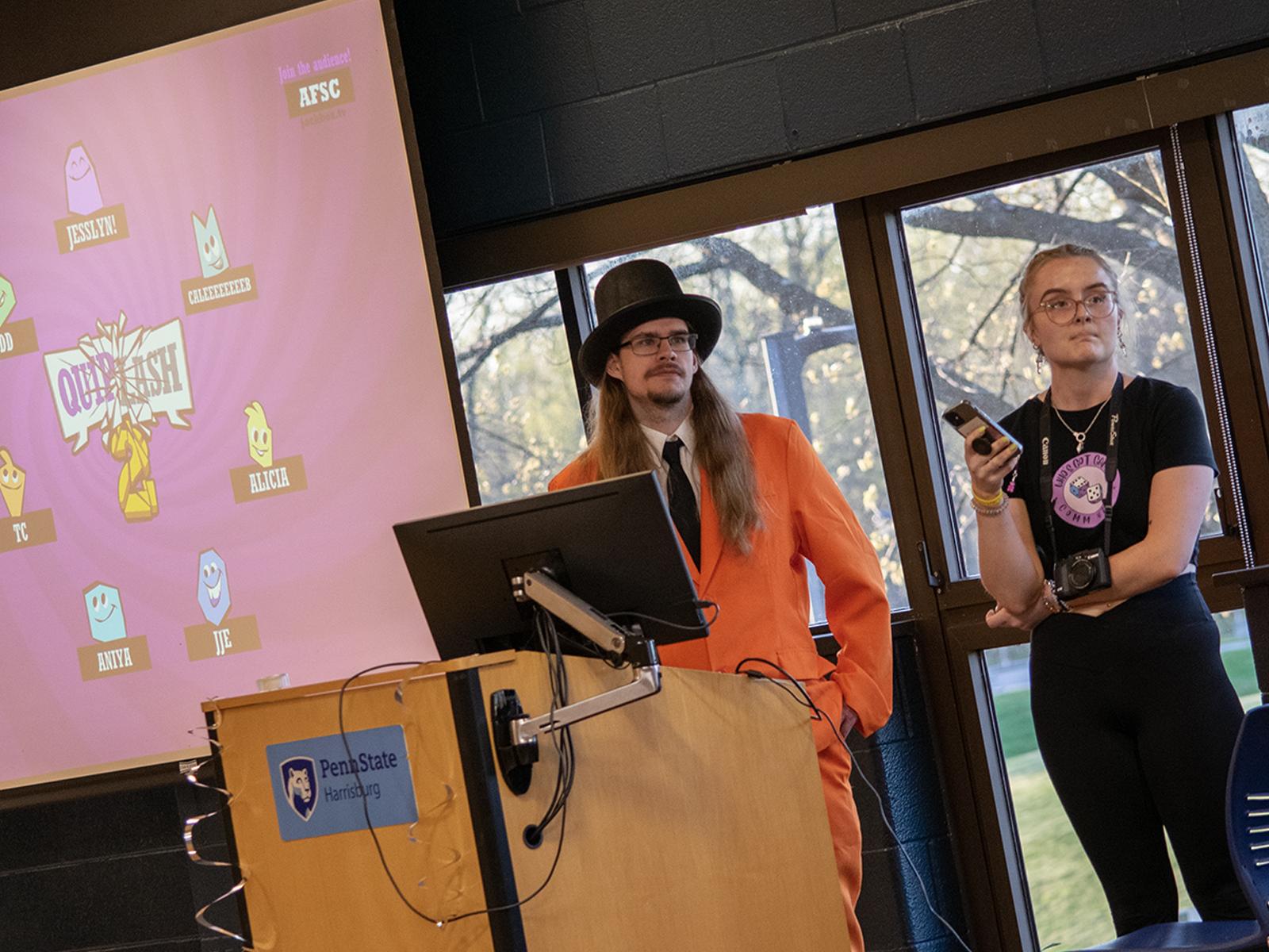 Two students stand next to a projector screen as they run games during a fundraiser 