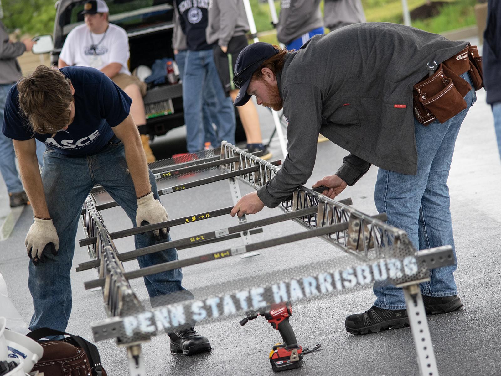 Two students work on a steel bridge during the ASCE competition
