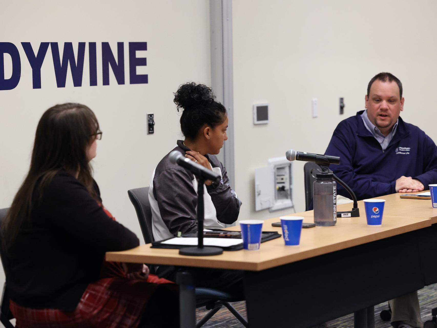 Three staff members sitting at a table with three microphones