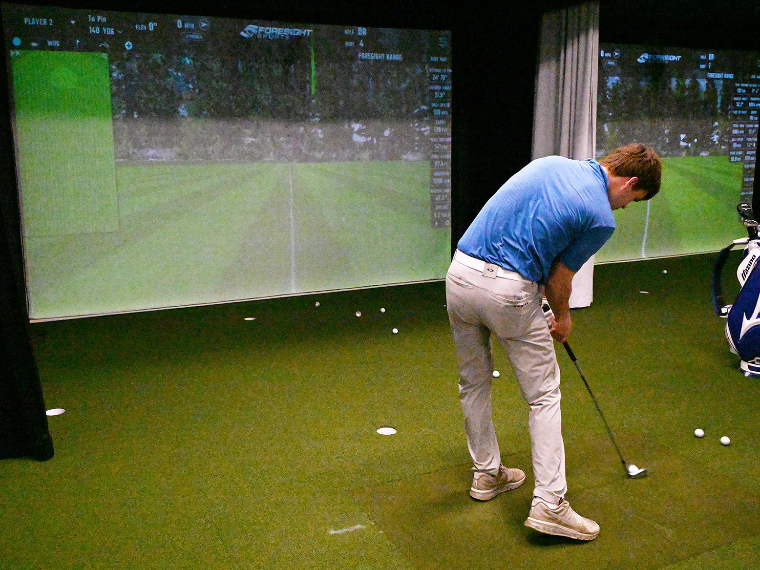 A golfer hits a golf ball toward a screen in the Golf Teaching and Research Center.