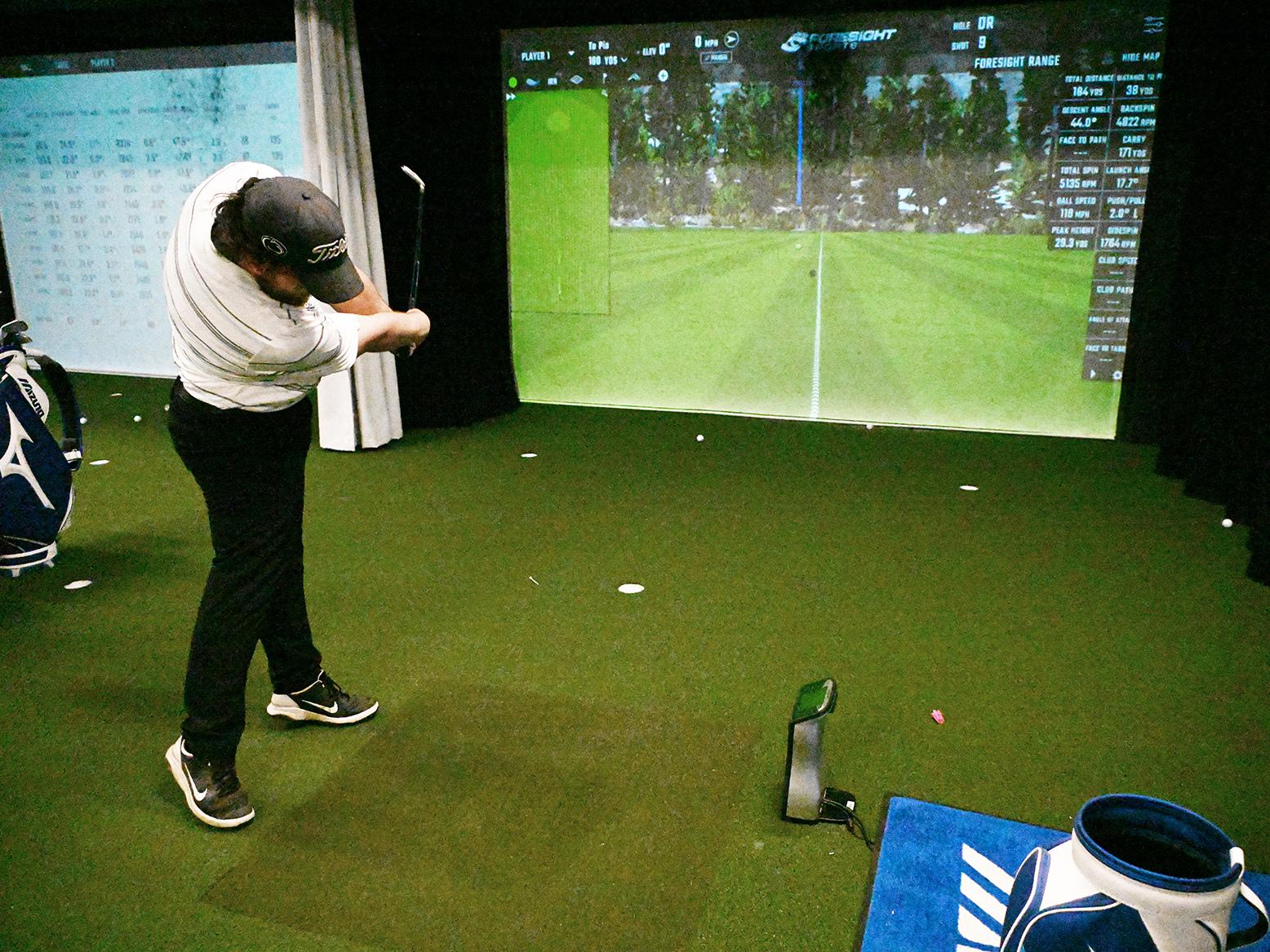 A golfer hits a ball toward a screen in the Golf Teaching and Research Center.