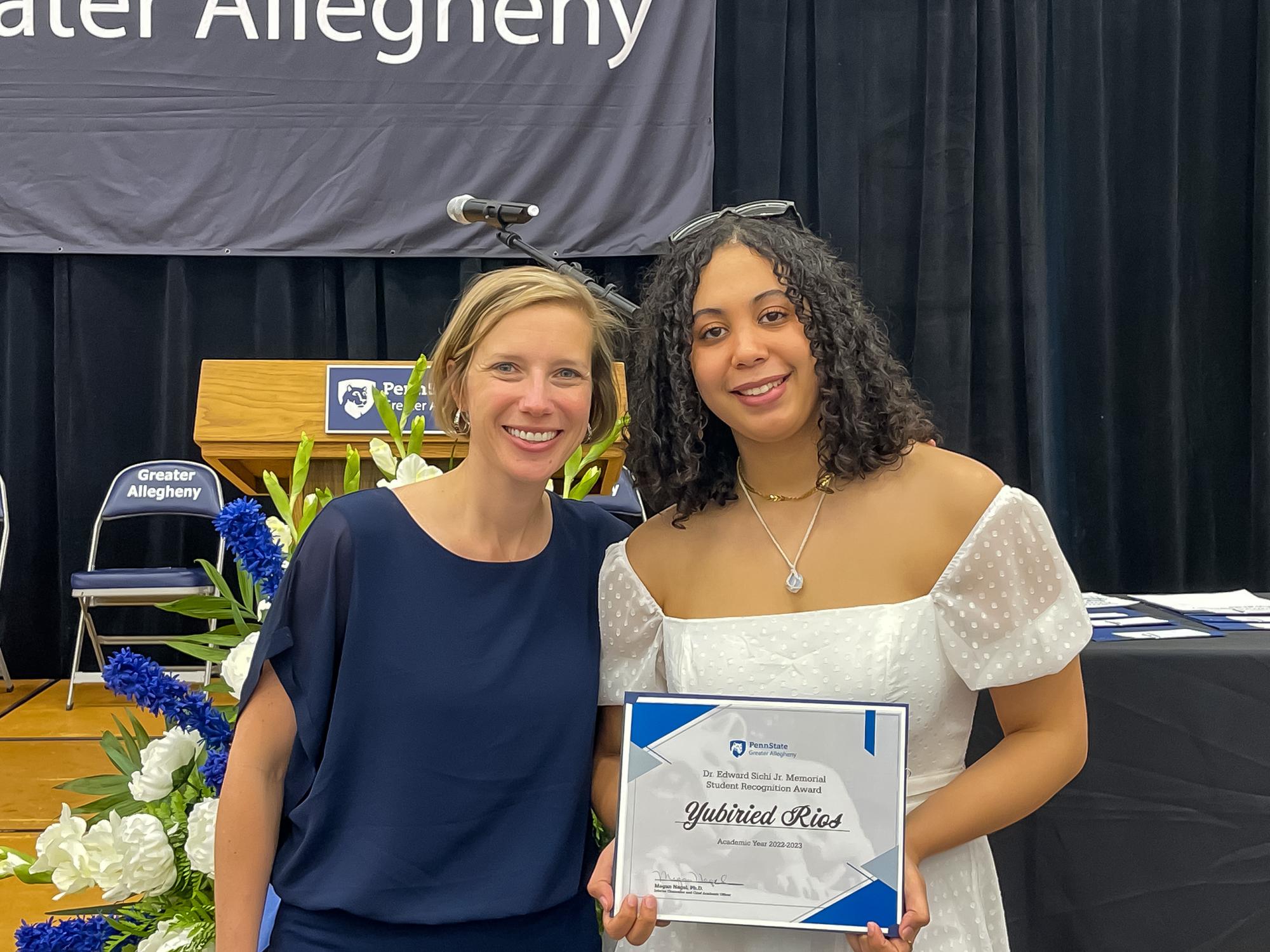 two people smiling with one holding an award