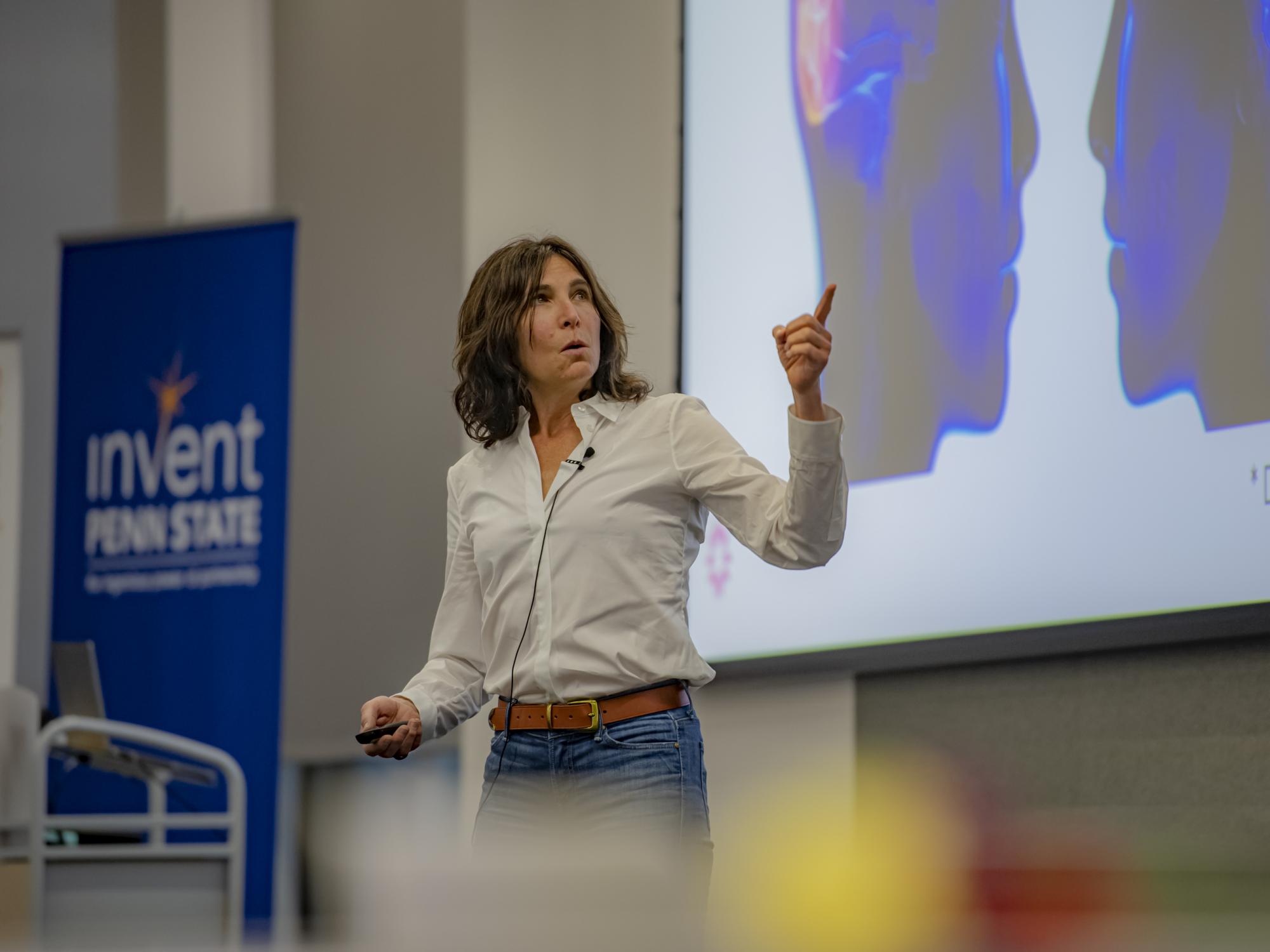 Photo of a woman in a white blouse pointing at a screen during a presentation.