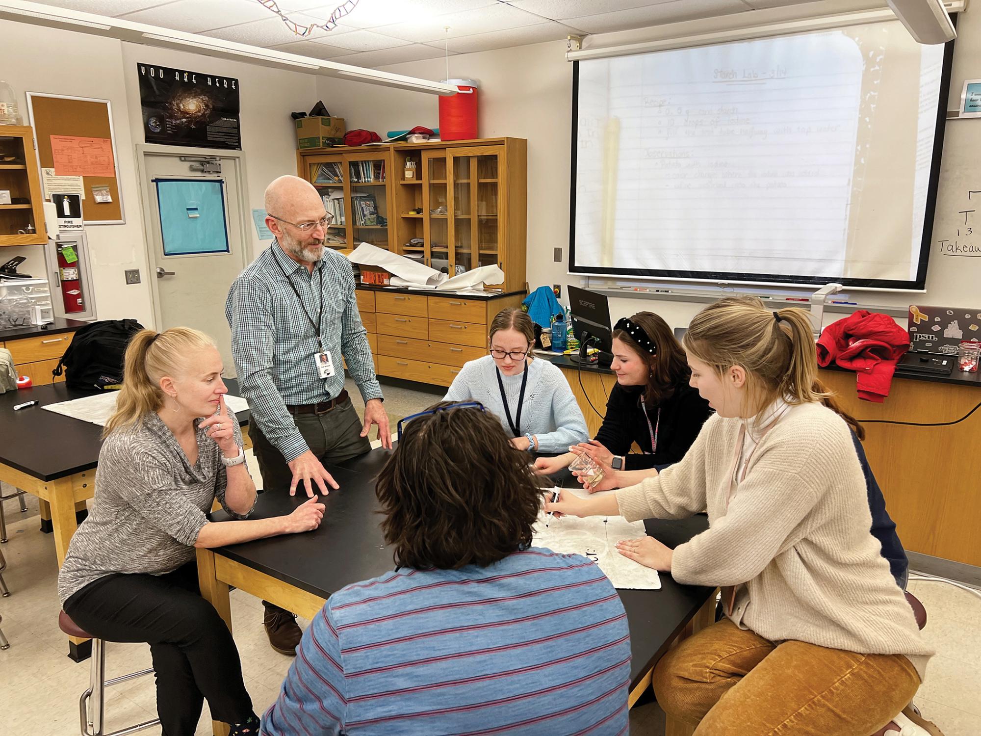 Scott McDonald leads a discussion with students seated around a table.