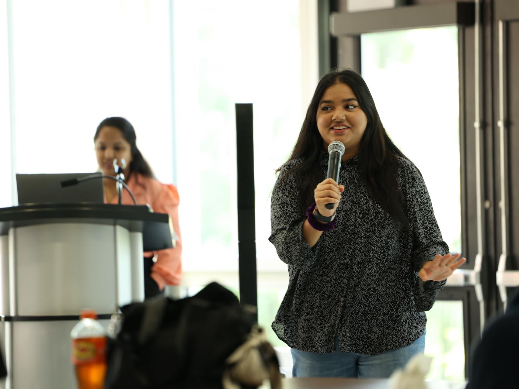 Girl holding a microphone with another girl at a podium