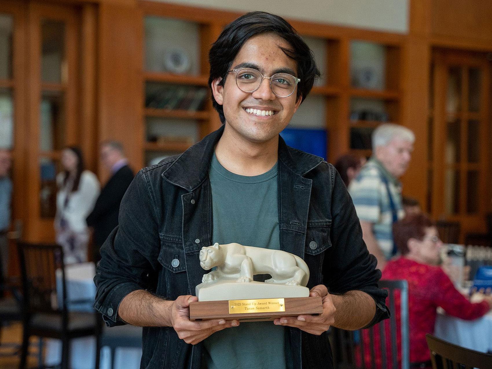 Taran Samarth holding a Stand Up Award resembling the Nittany Lion