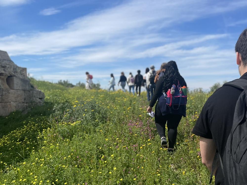 A group of Penn State students walking with their backs facing the camera through the fields of architectural remains at Kolona.