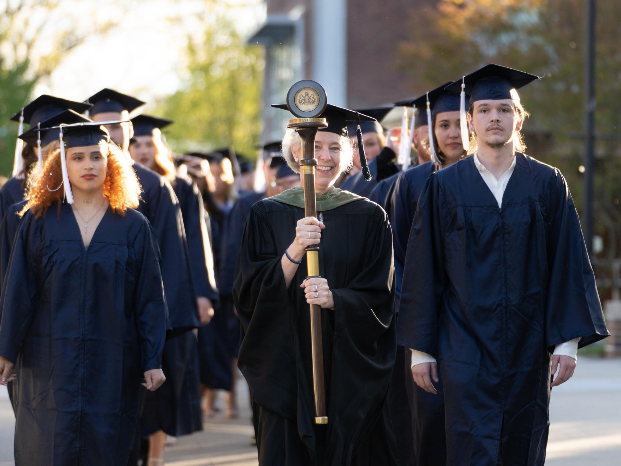 Two rows of students in caps and gowns processing down a sidewalk.