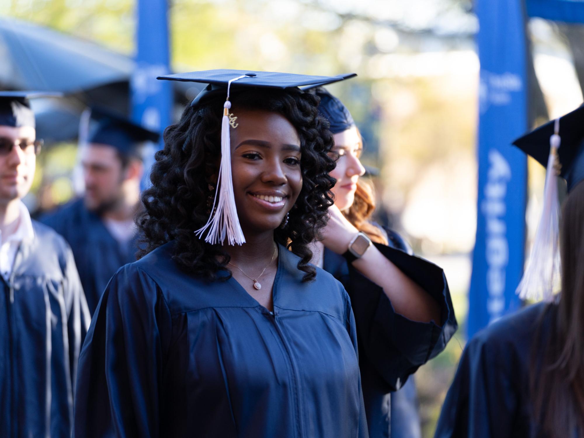 Female graduate in cap and gown smiling at camera.