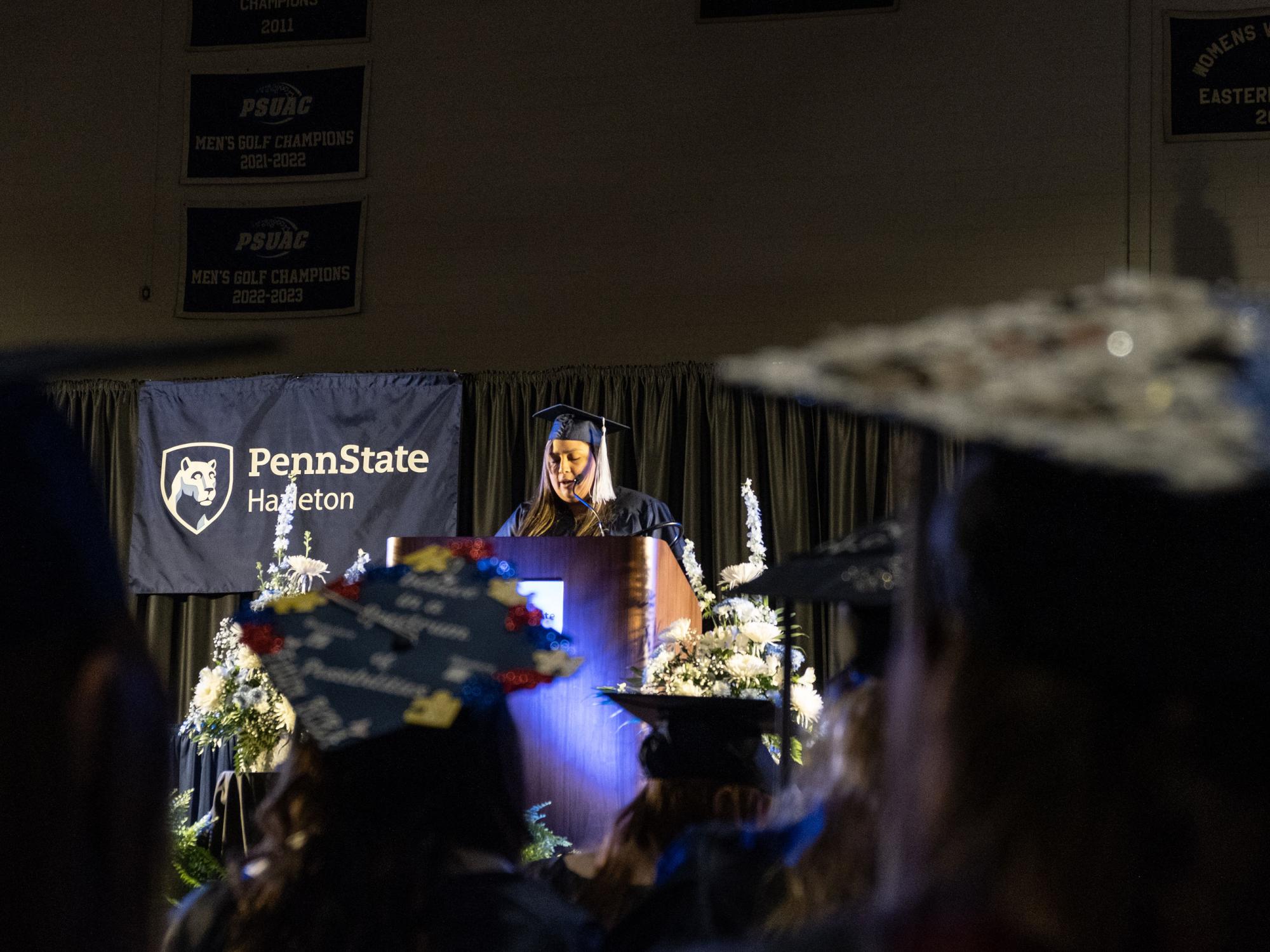 A woman in a cap and gown speaking from a podium on a stage.